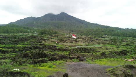 mount batur with lush green fields and an indonesian flag in the foreground, aerial view