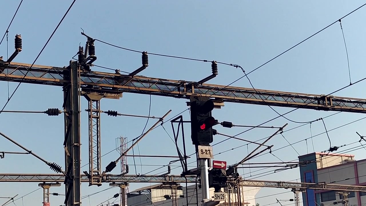 Close view of railway signal system with overhead electric lines and infrastructure, ideal for transportation documentaries, rail industry visuals, engineering, and transit content.