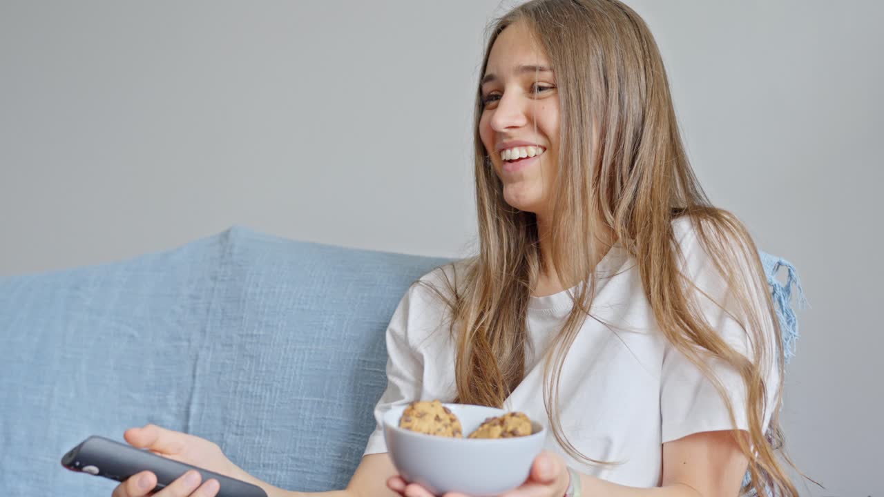 chica viendo comedia, sostiene galletas de chocolate y usando el control remoto de la tv, disparo estable