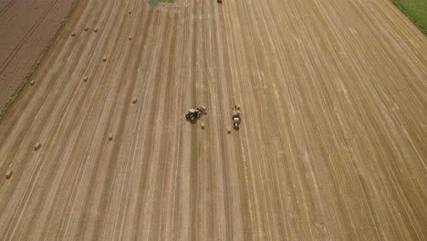 Maquinaria-Agrícola-De-Cosecha-De-Heno,-Tractor-En-El-Campo-De-Tierras-De-Cultivo-Agrícola-Que-Trabaja-Con-Fardos-De-Heno-De-Carga,-Vista-Aérea-Del-Trabajo-Agrícola