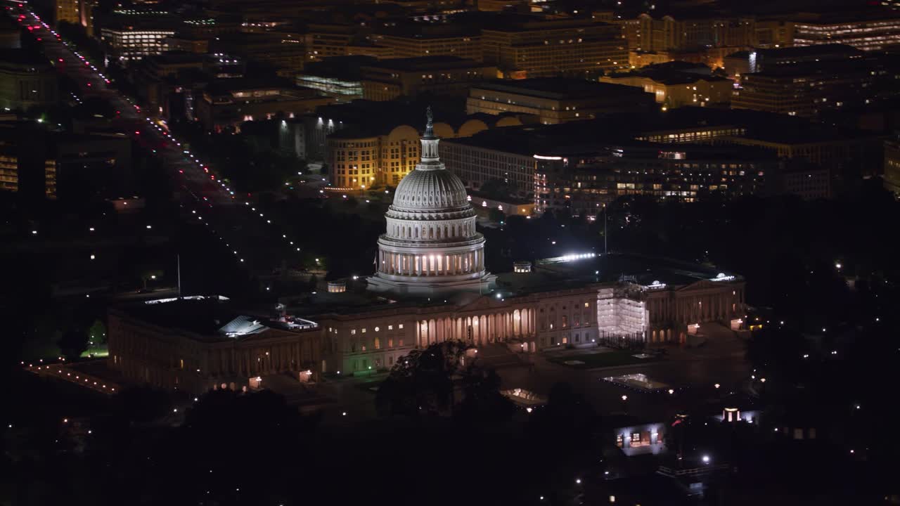 Tomada Aérea Noturna do Capitólio dos EUA Iluminado e Ruas Circundantes, Destacando sua Cúpula Icônica