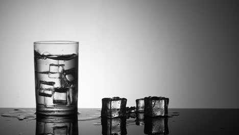 slow motion ice cube drops into glass with water