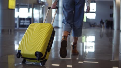 Stilvolle-Frau-Geht-Mit-Gelbem-Trolley-Koffer-Am-Leeren-Flughafen-Vorbei,-Niedrige-Halbansicht-Schlanker-Weiblicher-Beine-Und-Mittelgroße-Tasche-Mit-Rädern