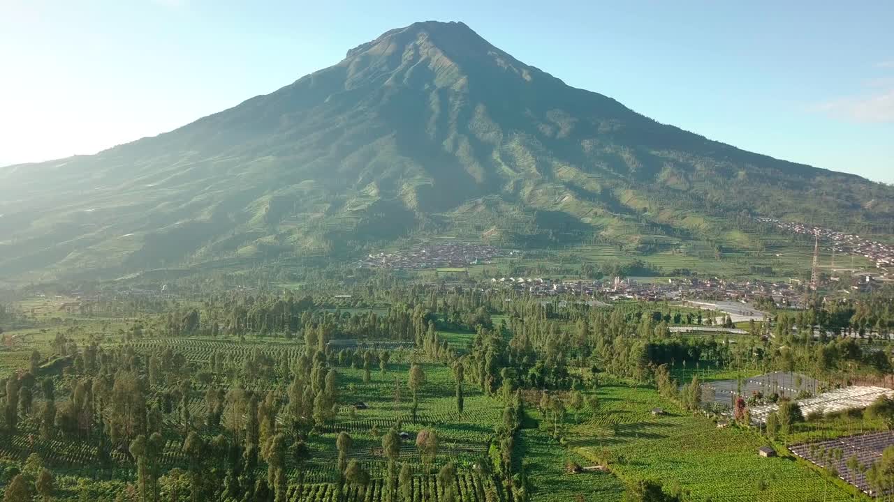 toma aérea hacia delante del volcán sumergido gunung y el campo verde con plantaciones en primer plano