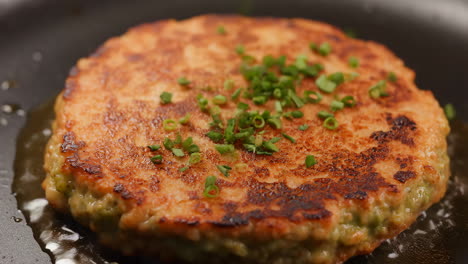 frying a golden-brown patty with chives in a pan