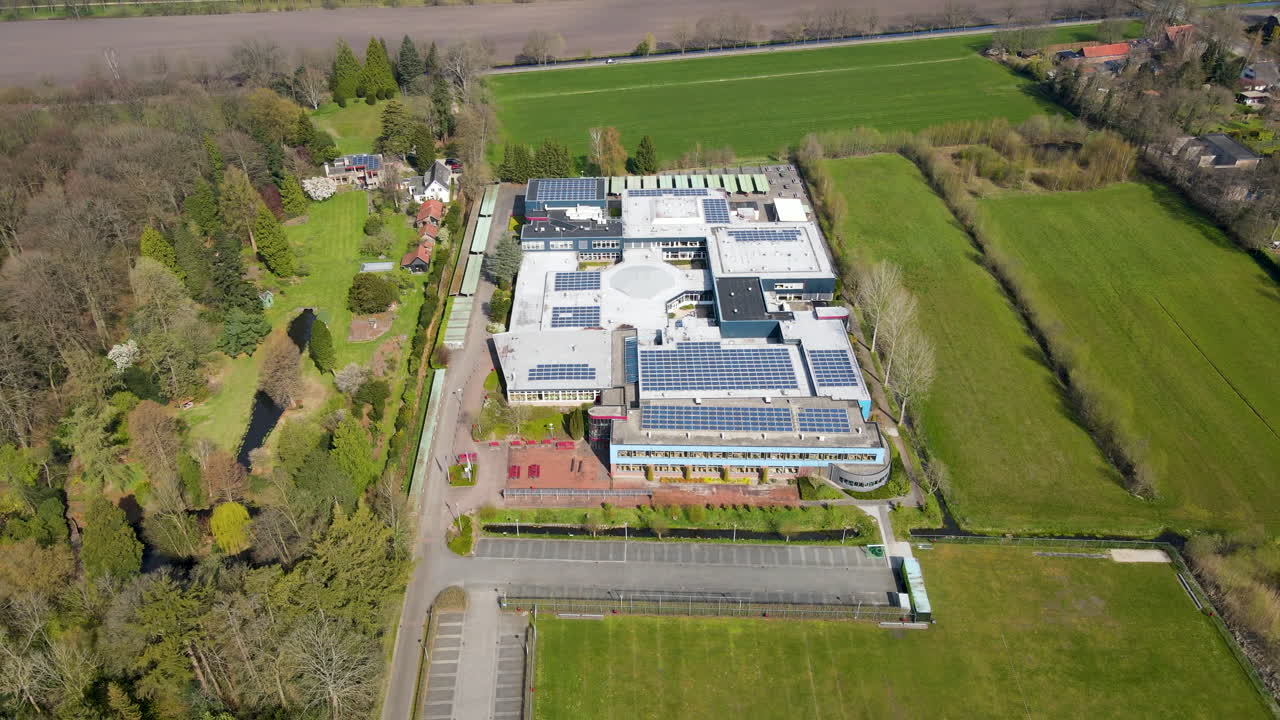 Luftfoto af et stort gymnasium med solpaneler på taget - drone flyver baglæns.