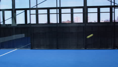 young woman playing padel tennis on blue indoor court, preparing to hit ball