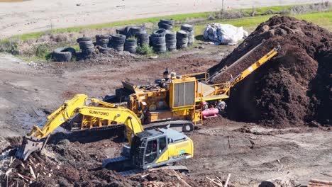 drone captures an excavator moving soil and mulch in a sunny outdoor setting. machinery operates efficiently in an industrial landscape