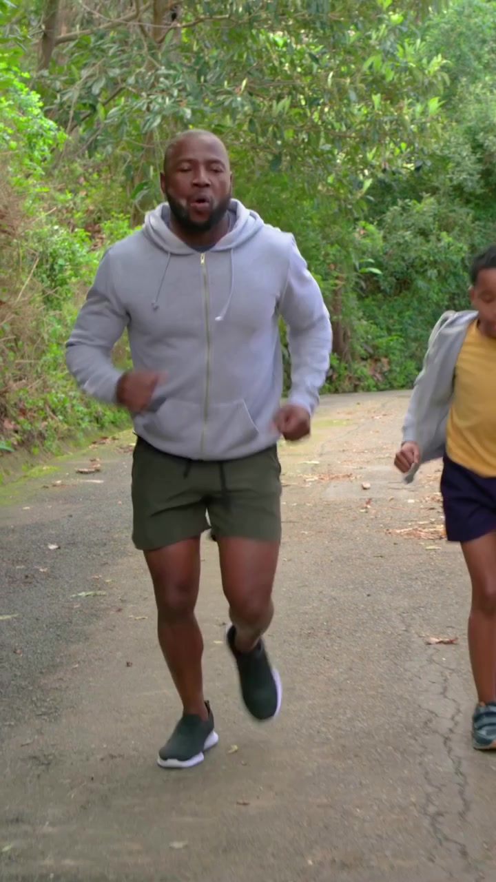 Video verticale: Arrivo su un sentiero pavimentato, papà in felpa con cappuccio e figlio che si riscaldano e poi fanno jogging per rafforzare il loro legame.