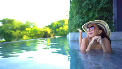 young asian woman resting on the ledge of an outdoor pool