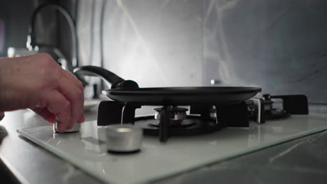 close-up shot of elderly woman's hand adjusting burner on modern gas stove. kitchen setting with sleek black and white design. focus on cooking and preparation actions in domestic environment