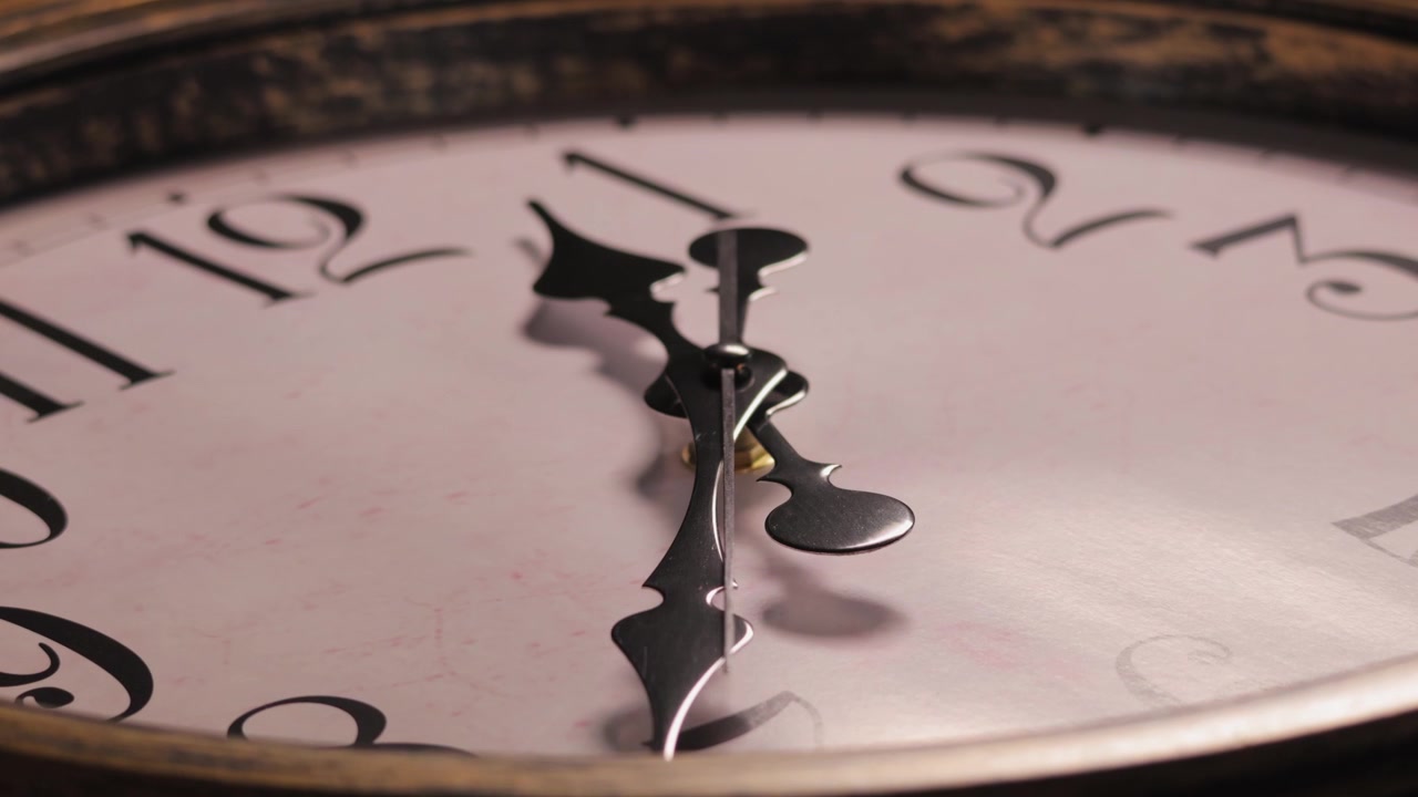 Close up static shot of a vintage wall clock. The thin second hand ticks steadily across the pink textured dial face showing the continuous passage of time.