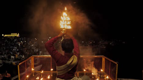 a back shot of a pujari or brahmin (hindu priest) holding fire lamps/ lantern/ diyas performing ganga pooja