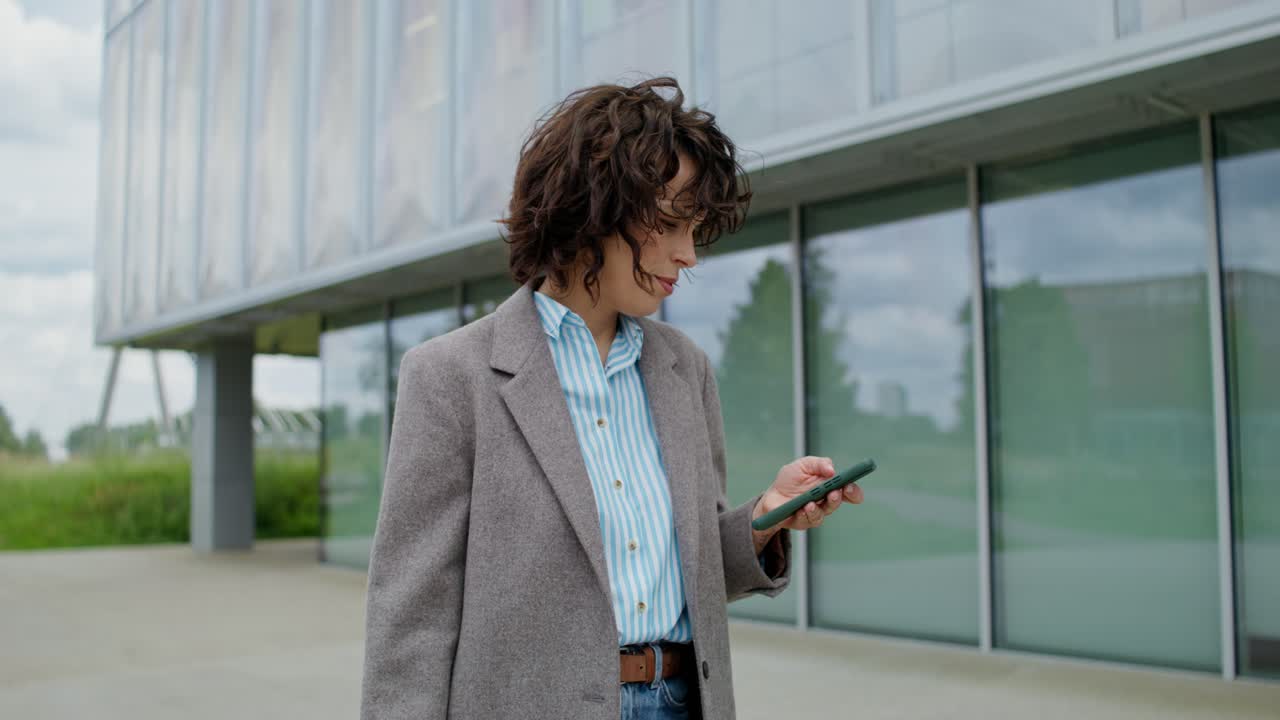 Kvinde bruger smartphone uden for en moderne kontorbygning