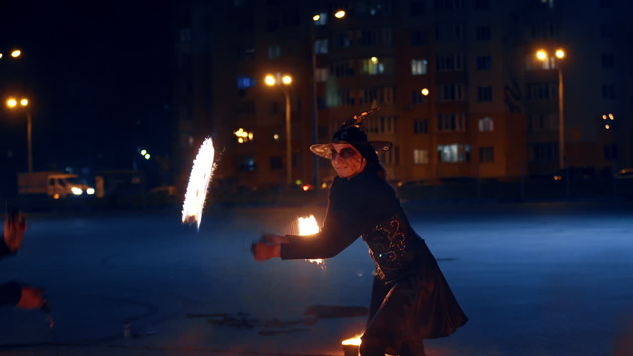 Woman in black dress, witch hat and spider web make up performing fire show. Show woman waves burning objects.