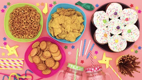 party food and decorations, cup cakes, straws, candles, balloons appear on the table - stop motion