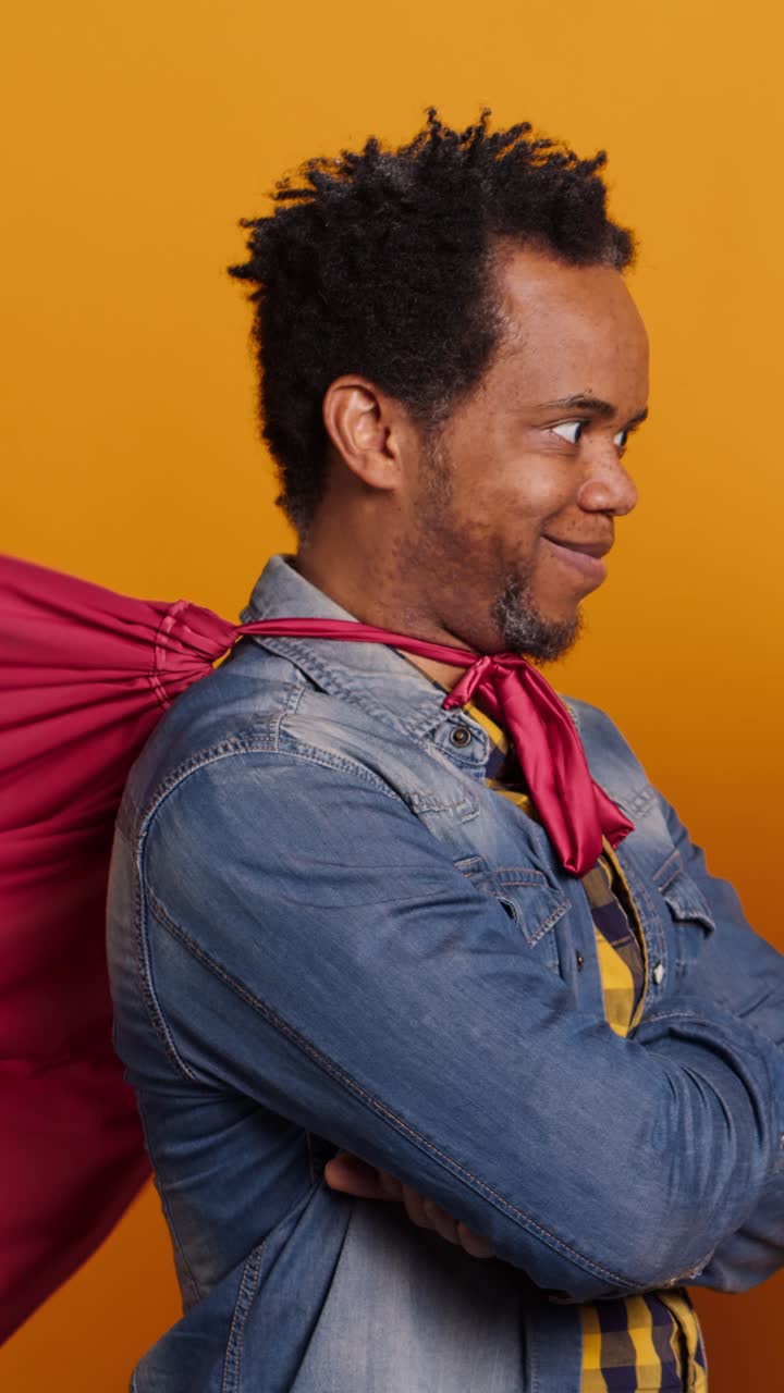 Hombre afroamericano seguro de sí mismo posando como superhéroe con capa roja