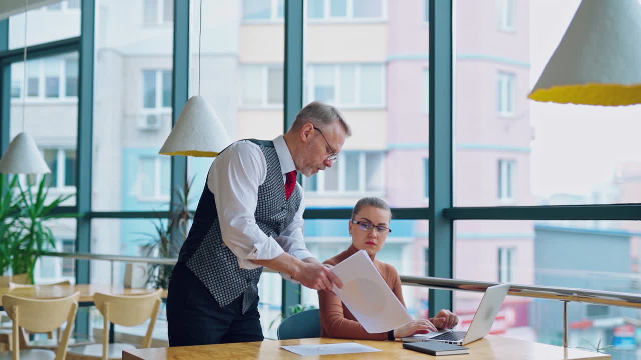 Mature entrepreneur with young secretary at work. Beautiful woman in glasses sitting in front of the computer and listenes to her boss. Slow motion.
