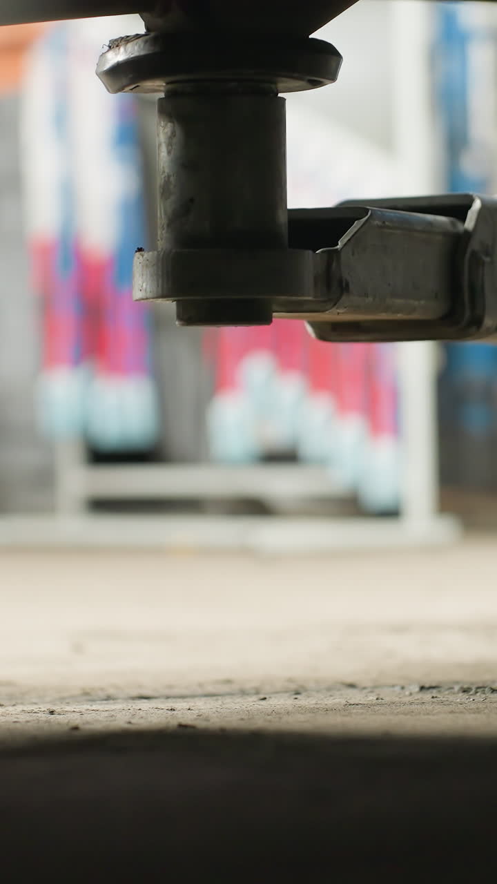 Close-up de elevador automotivo eletrônico elevando um veículo em uma oficina mecânica, com equipamento mecânico azul visível ao fundo, destacando a precisão e estabilidade do mecanismo de elevação.