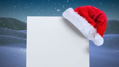 Animation-of-blank-card-with-copy-space-and-santa-hat-over-snow-falling-and-winter-scenery