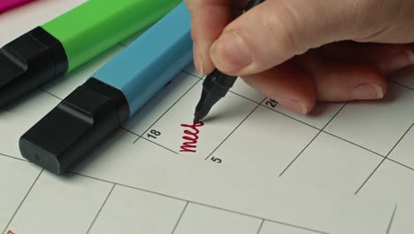 close up of female hand filling paper calendar with red marker writing a word meeting. planning concept