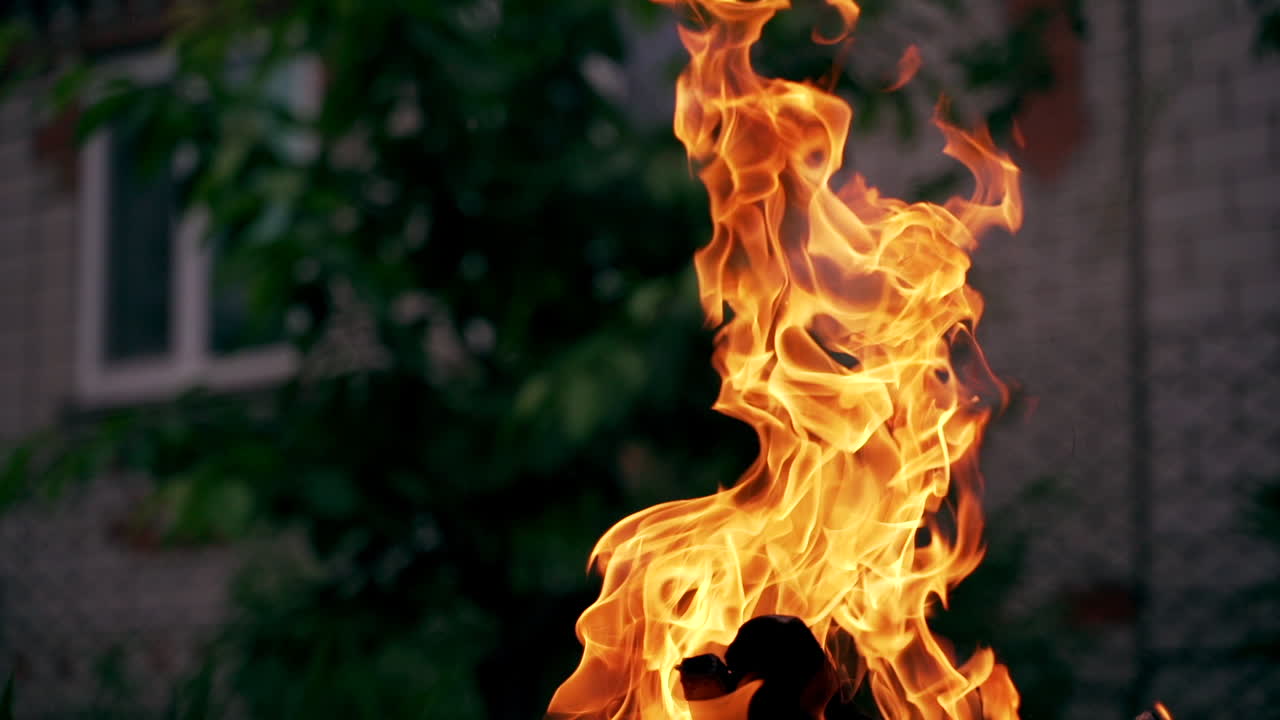 Bright flame of burning firewood outdoors. Natural texture of bright fire on blur building background in the evening.