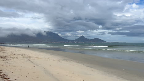 stunning early morning cape town clouds over table mountain beach landscape south africa seagull bird flying away people walking on beach low tide incredible coastline slow motion pan to the left