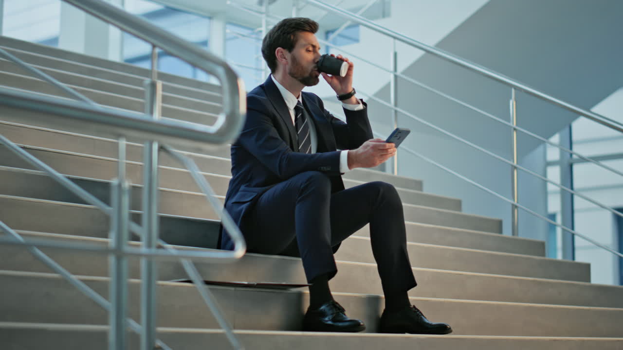 Relaxed manager looking smartphone sitting stairs with coffee. Thoughtful man