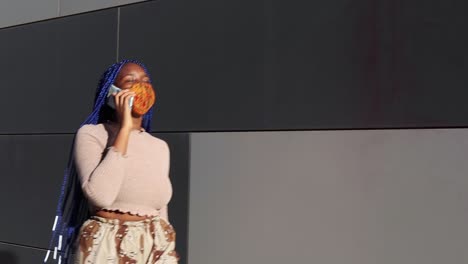 mujer negra con máscara hablando en un teléfono inteligente en la ciudad