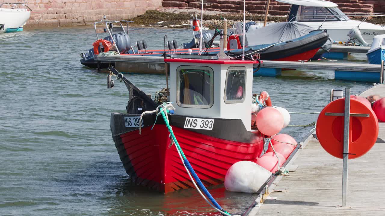 Red fishing vessel docked at marina, gentle water movement, bright daylight, stable camera, coastal setting