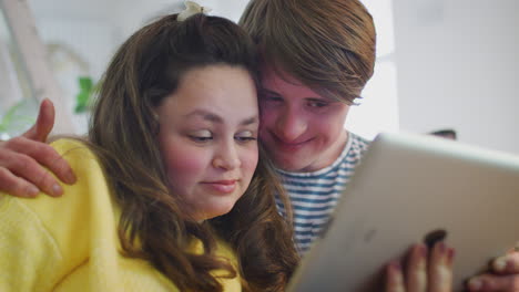 young downs syndrome couple sitting on sofa watching digital tablet at home