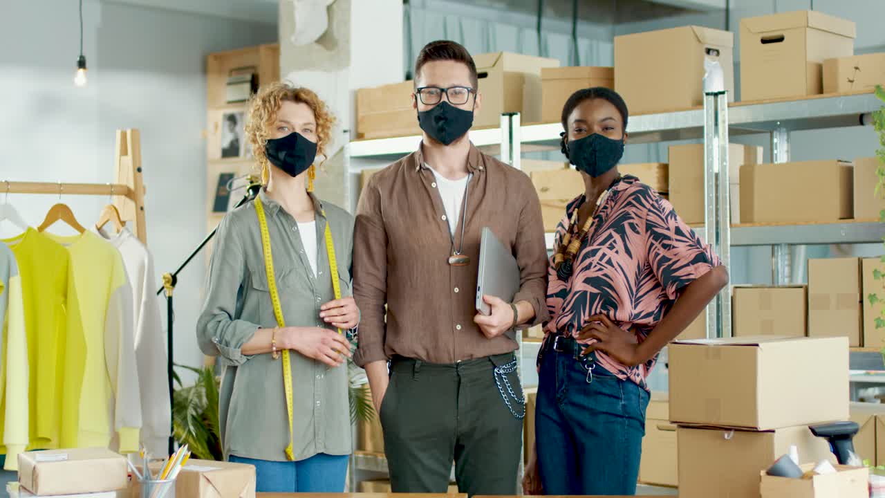 mujeres caucásicas y afroamericanas y hombre caucásico con máscaras y mirando la cámara en el almacén de la tienda de ropa