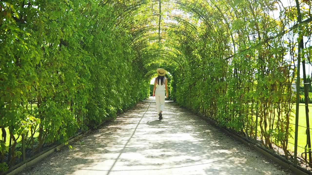 Elegant woman walks in sunlit green tunnel, evoking calm and natural harmony