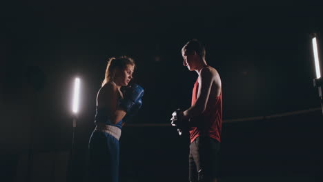 boxeadora golpeando unos guantes de enfoque con guantes de boxeo en un gimnasio ahumado