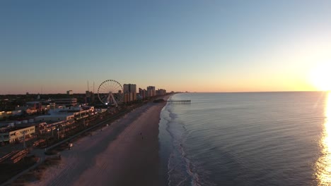 Vista-Aérea-Del-Amanecer-De-Myrtle-Beach-En-La-Tira-Con-Rueda-Farris-Y-Muelle-En-Segundo-Plano