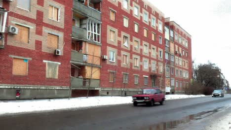 cars passing red brick apartment building in sloviansk, ukraine with boarded windows