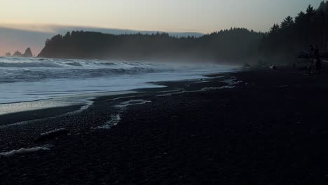 stunning tilting up shot of a peaceful sunset at the famous ruby beach in forks, washington with sea foam left from small waves along the pacific coastline and cliffs of pine trees on a summer evening
