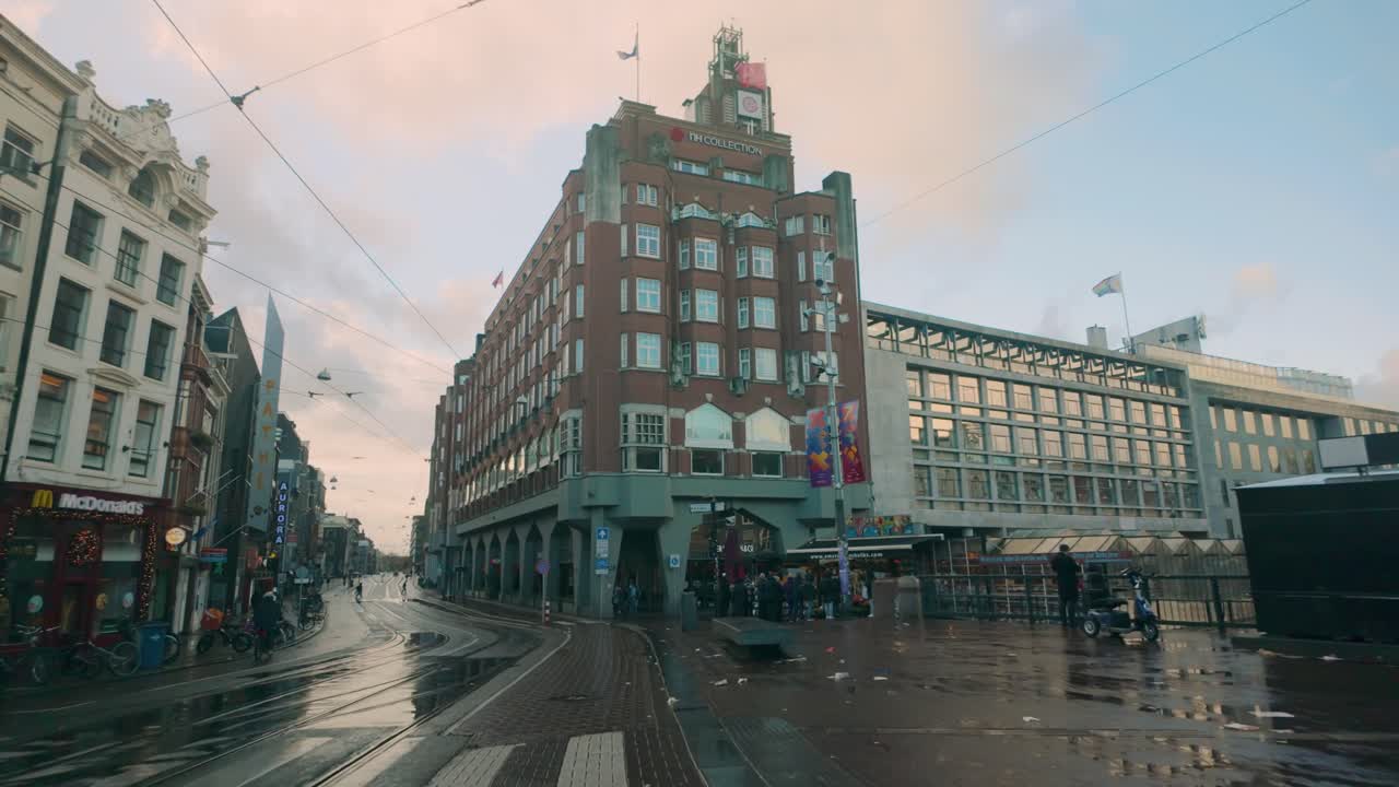 Morning scene in Amsterdam with iconic brick architecture, wet streets, and soft pastel skies. A classic blend of historic and modern buildings highlights urban charm and rainy tranquility.
