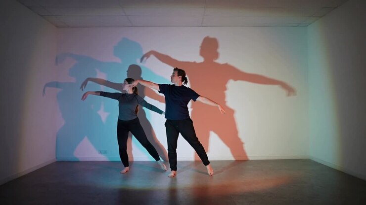 Dance duet initiating cue, stepping, rotating, reaching, cyan-red lights casting layered shadows