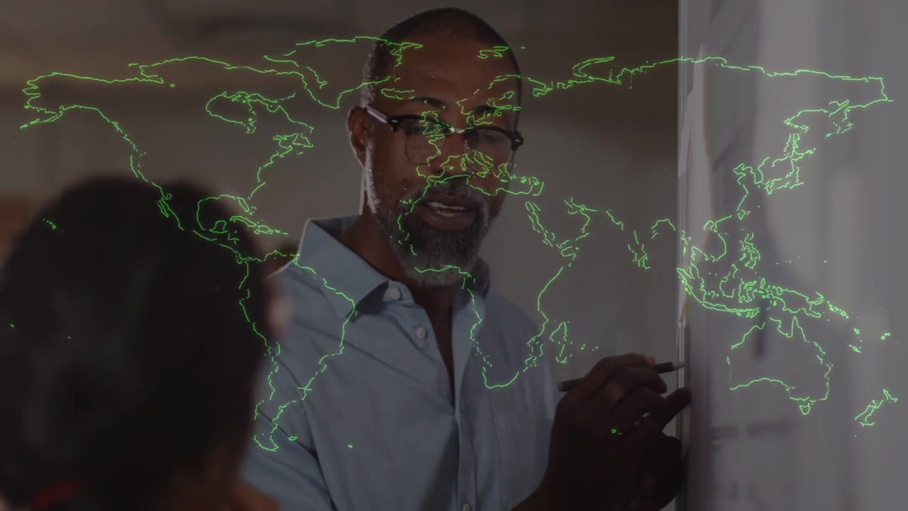 Homem de camisa azul-clara e óculos, escrevendo em um quadro branco com um marcador durante uma reunião, com um mapa verde.