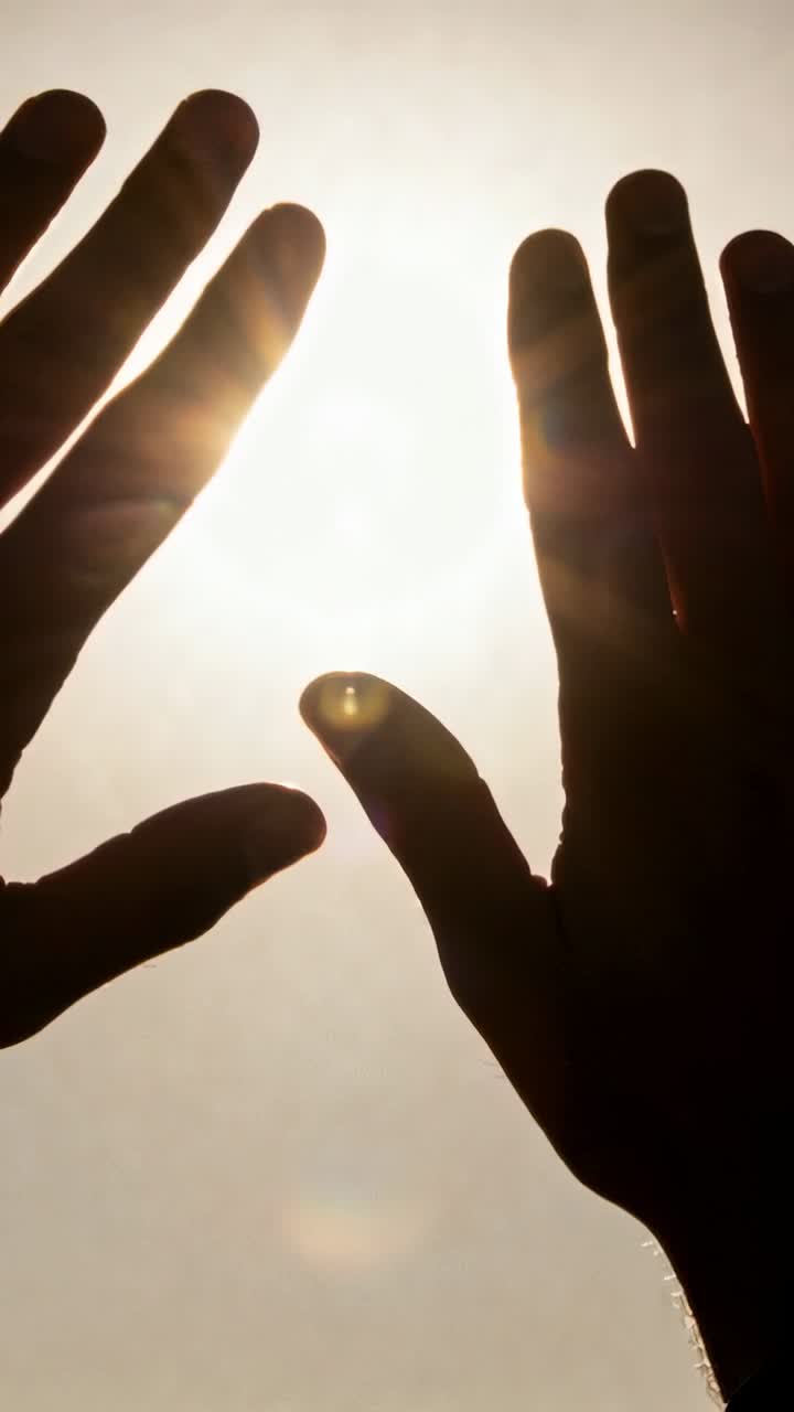 Video verticale: Mani che si aprono reagendo a un raggio di sole nel cielo blu, creando bagliori dell'obiettivo, un anello di metallo.