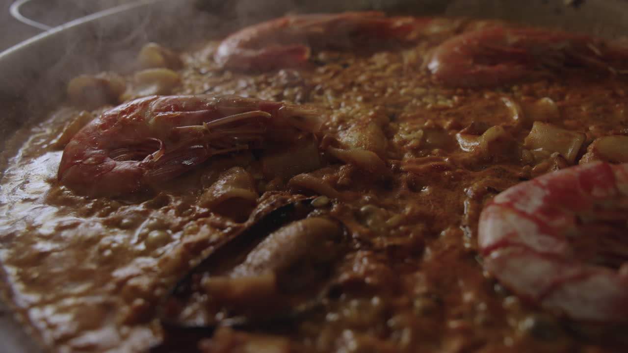 Primo piano di una paella valenciana ai frutti di mare che sobbolle al rallentatore con bolle di vapore e un leggero movimento della camera