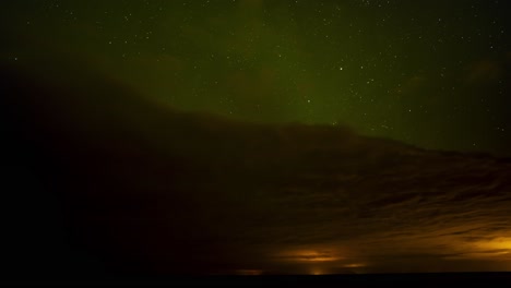 beautiful time lapse of green northern lights above dark clouds with a starry night sky with shooting stars