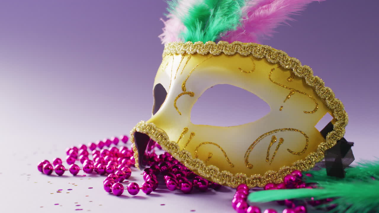 video de una máscara de mascarada de carnaval con plumas y cuentas de mardi gras rosas, sobre fondo púrpura