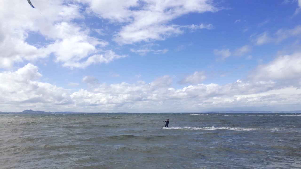 un kitesurfista que pasa a gran velocidad, cerca de la costa, en un ventoso día de verano | playa de portobello, edimburgo | filmado en hd a 24 fps cinemáticos