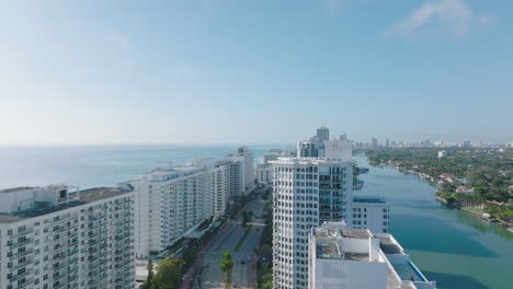 Multilane-trunk-road-leading-between-tall-luxury-apartment-buildings-along-sea-coast.-Forwards-fly-above-town-development.-Miami,-USA