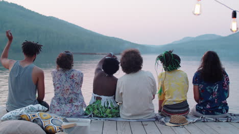 diverse friends sitting on lake pier and chatting in evening