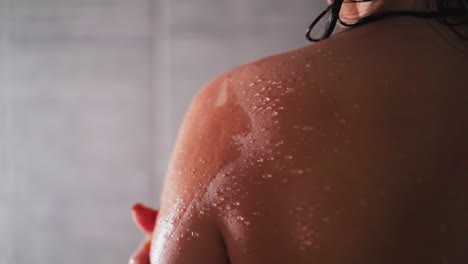 woman applies scrub on shoulder in shower unit closeup. lady exfoliates dry skin with homemade cosmetic product in bathroom. spa relaxation at home