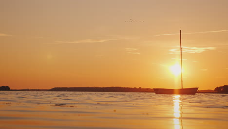 Un-Barco-De-Pesca-Solitario-En-La-Superficie-Del-Espejo-Del-Lago,-El-Sol-Poniente-Ilumina-Todo-Con