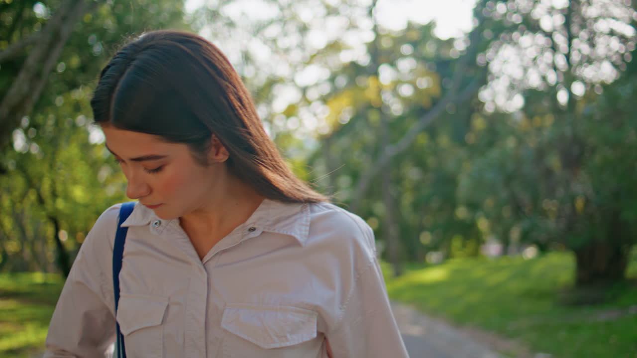 걸어다니는 소녀가 전화에 응답하고 그린 파크 클로즈업에서 가방에서 스마트폰을 꺼내고 있습니다.